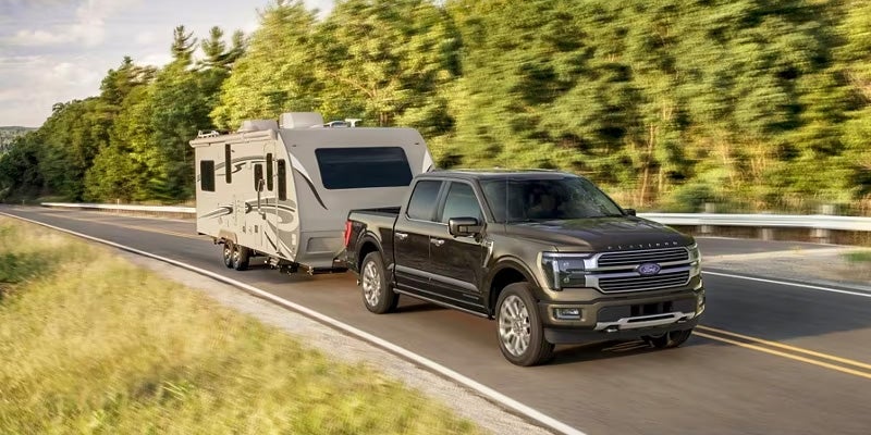 A grey 2024 Ford F-150 hauling a camper down the highway on a sunny day
