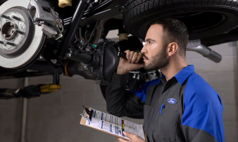 Ford technician checking under a car with flashlight